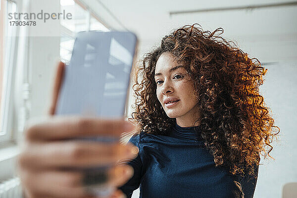 Junge Frau mit lockigem Haar nutzt Smartphone