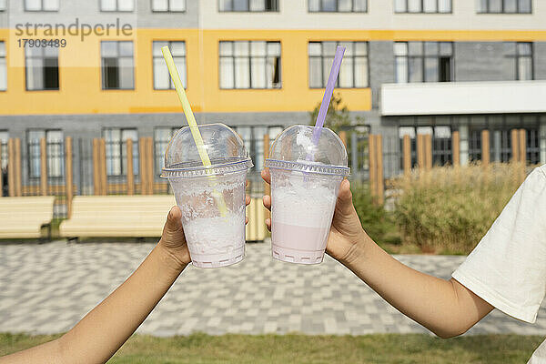 Hände von Mädchen  die an einem sonnigen Tag Einwegbecher mit Milchshakes vor dem Gebäude halten