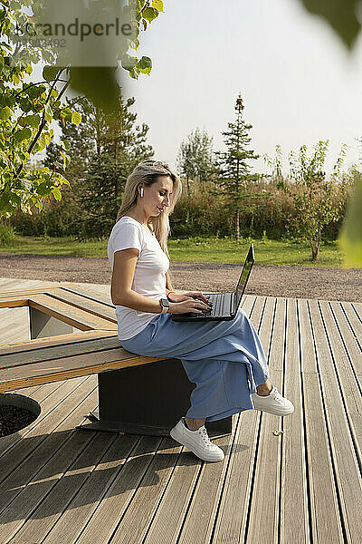 Freiberufler arbeitet am Laptop und sitzt auf einer Bank im Park