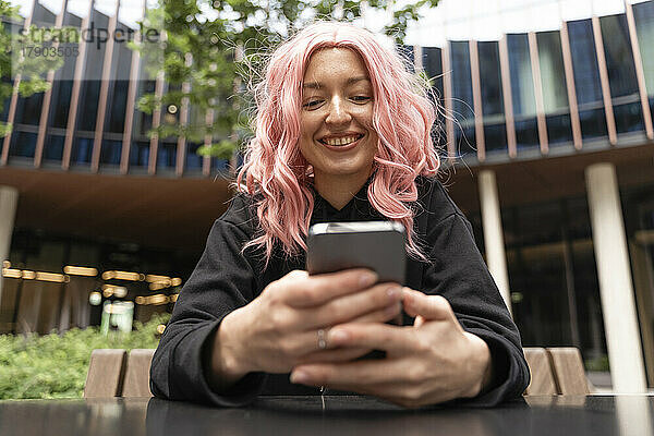 Glückliche Frau mit rosa Haaren  die Textnachrichten über das Smartphone sendet