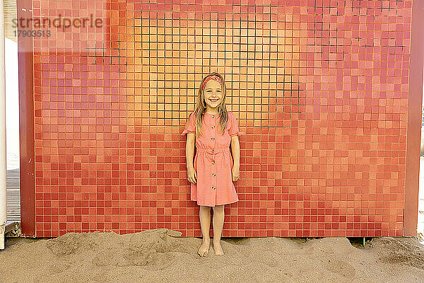 Glückliches süßes Mädchen  das vor der Wand am Strand steht