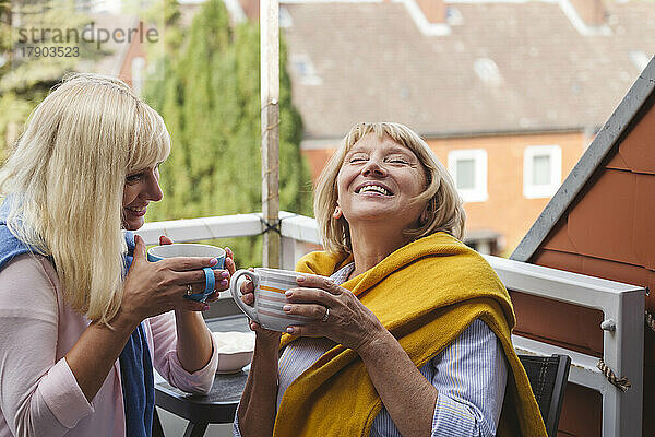 Glückliche Mutter und Tochter sitzen zusammen mit Kaffeetassen auf dem Balkon