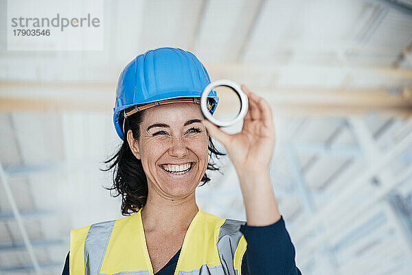 Glücklicher Ingenieur trägt reflektierende Kleidung und hält ringförmiges Objekt in der Fabrik