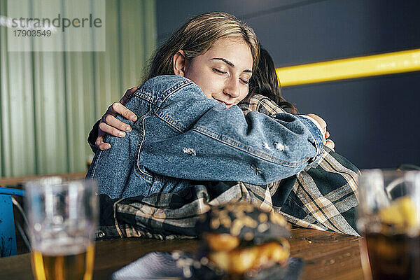 Young lesbian couple hugging each other at table in restaurant