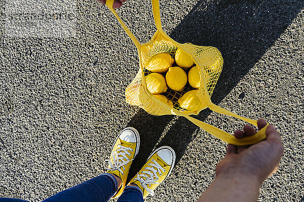Frau steht auf der Straße und öffnet Netzbeutel mit Zitronen