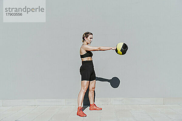 Junge Frau trainiert an einem sonnigen Tag mit Medizinball