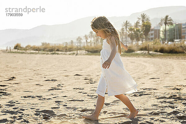 Mädchen mit langen Haaren geht an einem sonnigen Tag am Strand spazieren
