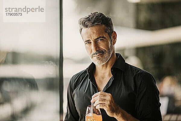 Handsome mature man by glass wall holding drink
