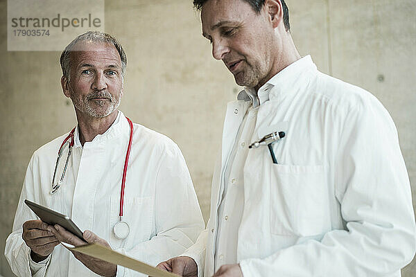 Leitender Arzt mit Tablet-PC von Kollege beim Blick auf die Akte im Krankenhaus