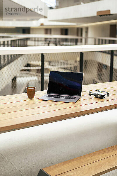 Laptop und Drohne mit Kaffeetasse auf dem Tisch im Büroflur