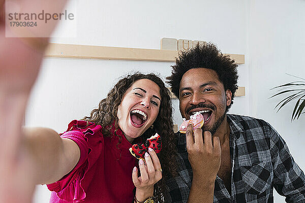 Glückliche junge Geschäftsfrau genießt Donut mit Kollege in der Cafeteria