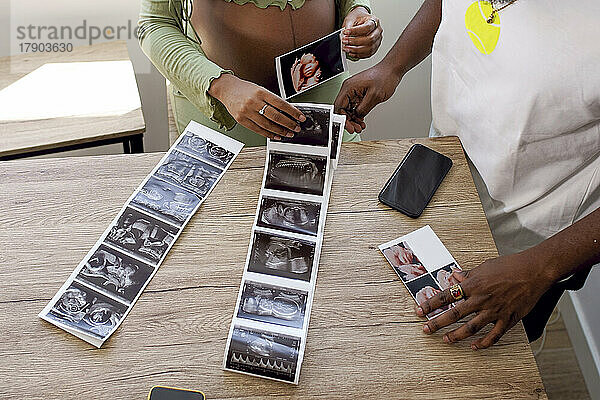 Schwangere Frau von Mann mit Ultraschallfotos des Babys auf dem Tisch