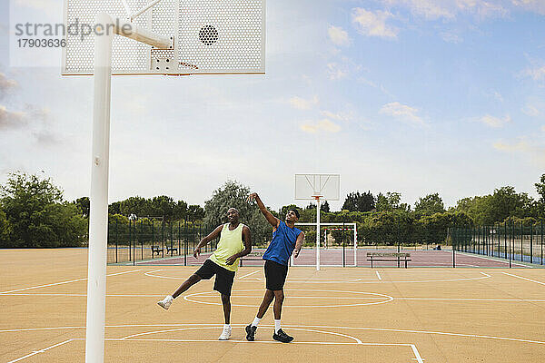 Junger Mann wirft Basketball im Korb und spielt mit Vater auf dem Sportplatz