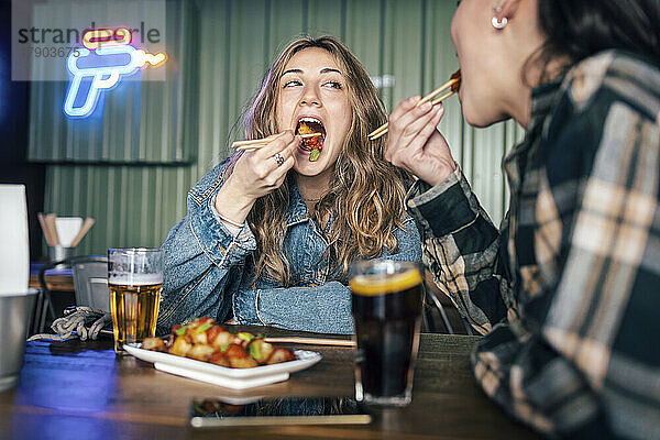 Junges lesbisches Paar isst Essen mit Stäbchen im Restaurant