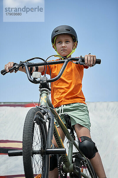 Entschlossener Junge sitzt auf BMX-Fahrrad im Skateboardpark