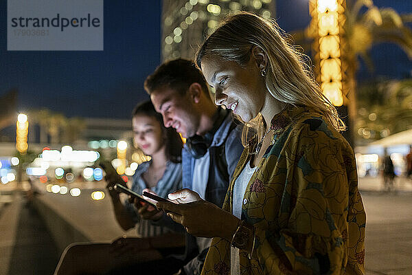 Lächelnde Frau  die nachts mit Freunden im Internet surft und mit Freunden sitzt