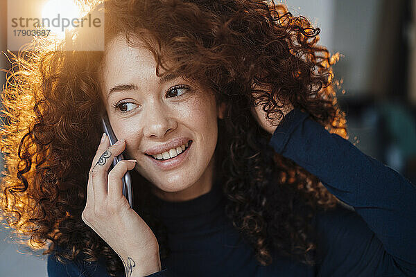 Lächelnde schöne Frau mit der Hand im Haar  die mit dem Handy spricht