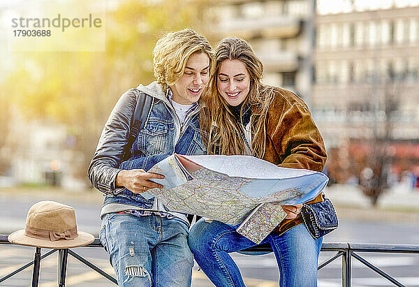 Lächelnder Mann und Frau  die auf dem Geländer sitzen und auf die Karte schauen