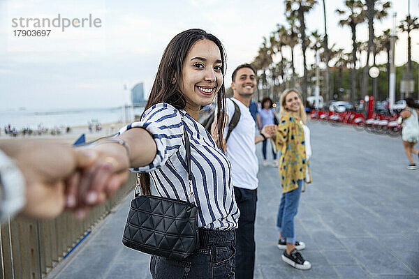 Lächelnde junge Frau hält Händchen von Freunden und genießt die Promenade