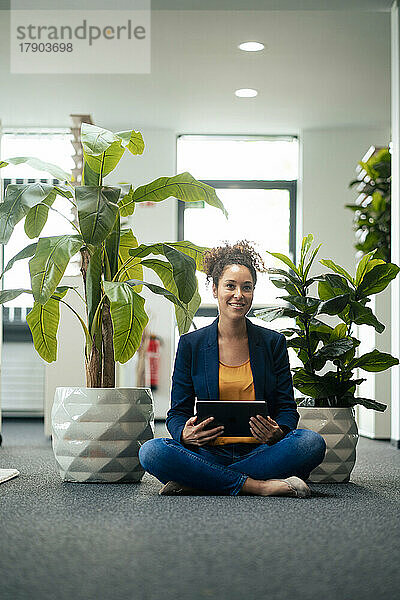 Lächelnde Geschäftsfrau mit Tablet-PC sitzt im Büro