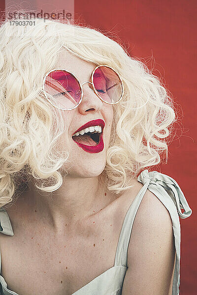 Fröhliche blonde Frau mit Sonnenbrille vor rotem Hintergrund