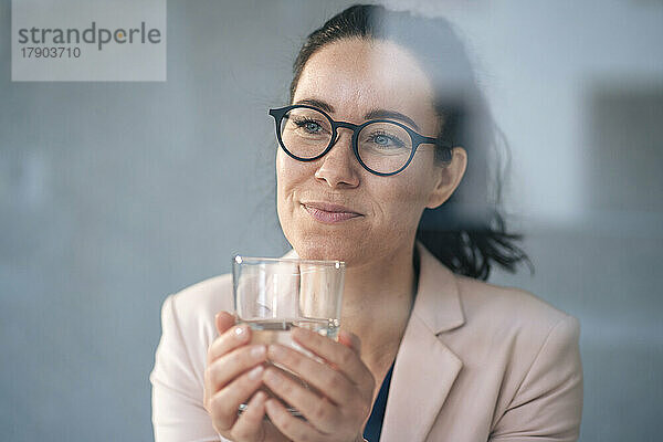Nachdenkliche Geschäftsfrau hält Trinkglas vor der Wand