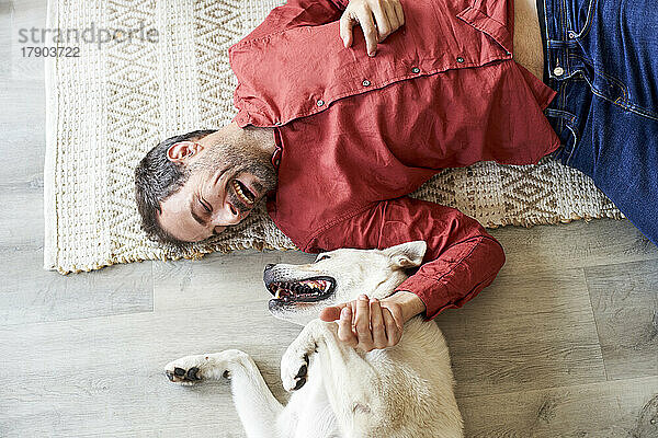 Happy man lying on carpet with dog on floor