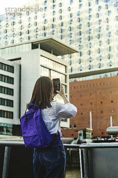 Frau mit Rucksack fotografiert Elbphilharmonie per Smartphone  Hafencity  Hamburg  Deutschland