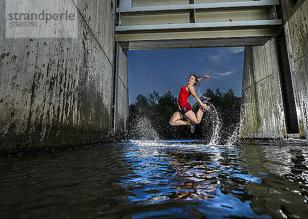 Aktive junge Frau springt in der Abenddämmerung über Wasser