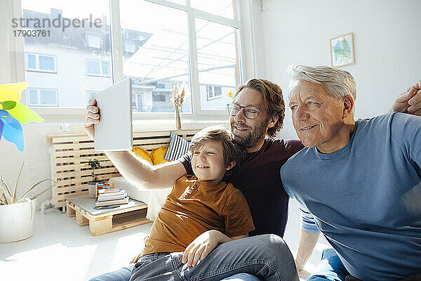 Lächelnder Mann  der zu Hause ein Selfie mit Sohn und Vater über einen Tablet-PC macht