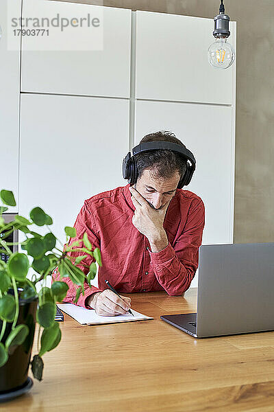 Geschäftsmann mit kabellosen Kopfhörern schreibt zu Hause