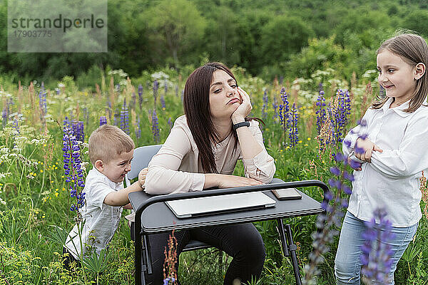 Müde Mutter mit Kindern sitzt auf der Wiese