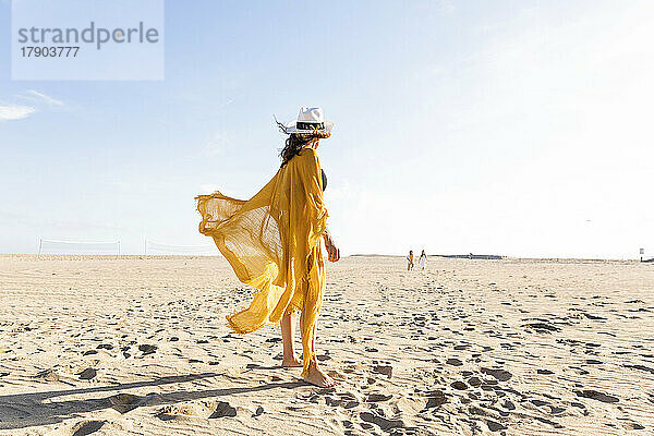 Reife Frau mit Hut steht an einem sonnigen Tag am Strand