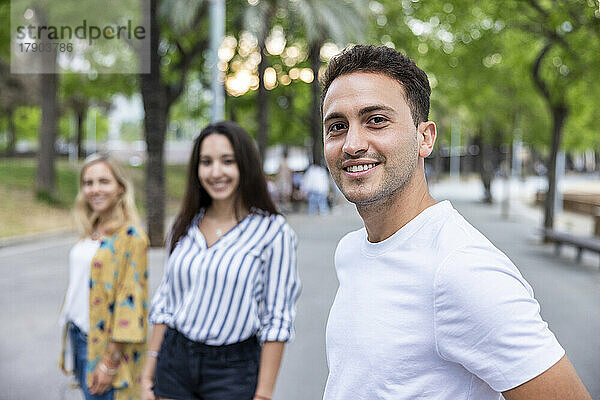 Smiling young man standing in front of friends at park