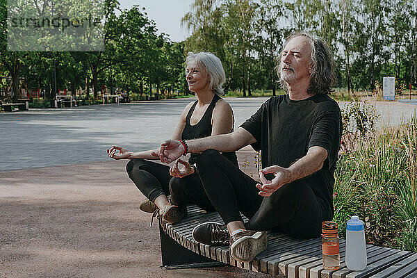 Paar sitzt auf Bank und meditiert im Park