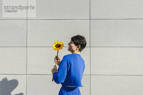 Glückliche Frau mit Sonnenblume  die an einem sonnigen Tag vor der Wand steht