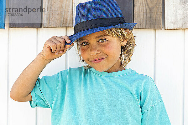 Lächelnder süßer Junge mit Hut vor einer Holzwand