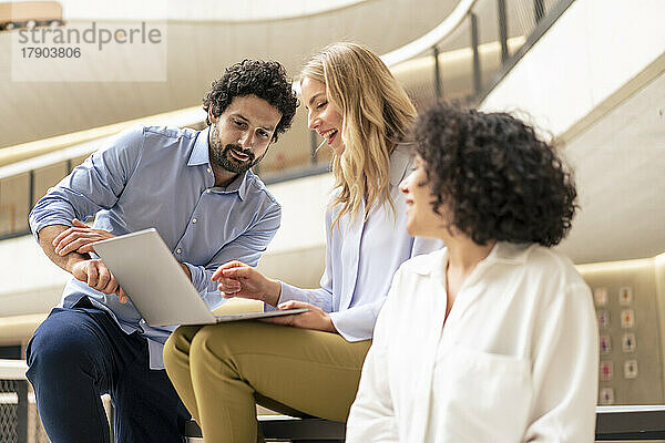 Glückliche blonde Geschäftsfrau diskutiert am Laptop mit Kollegen im Flur