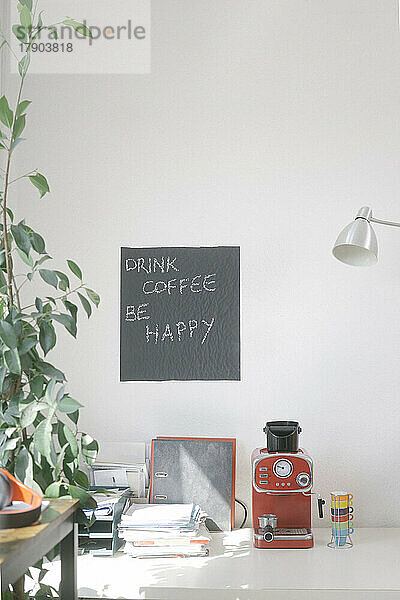 Kaffeemaschine und Dokumente per handschriftlichem Zitat an der Wand im Büro