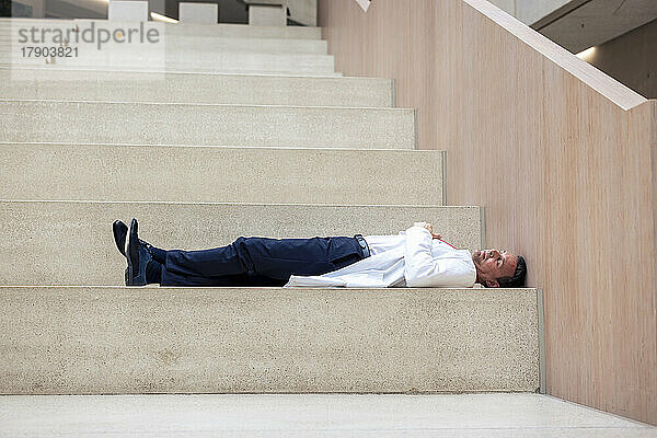 Overworked mature doctor lying on step in hospital