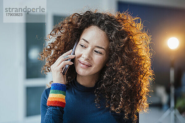 Lächelnde junge Frau mit lockigem Haar  die auf dem Smartphone spricht