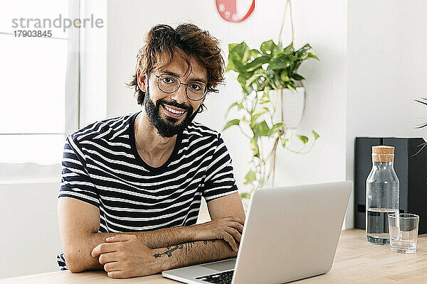 Glücklicher Mann sitzt mit Laptop im Heimbüro