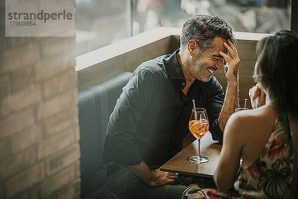 Glücklicher Mann mit Getränk  der neben seiner Freundin im Restaurant sitzt