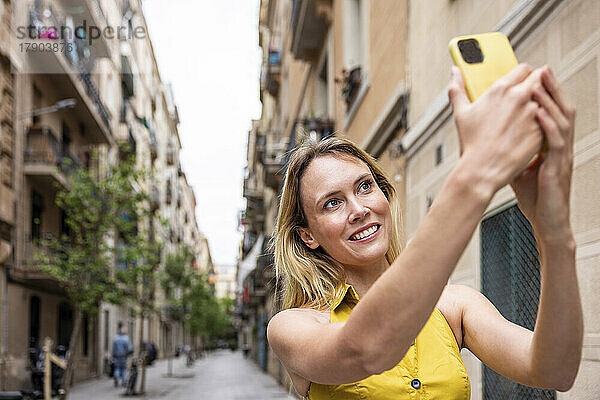 Lächelnde Frau  die in einer Gasse ein Selfie mit ihrem Smartphone macht