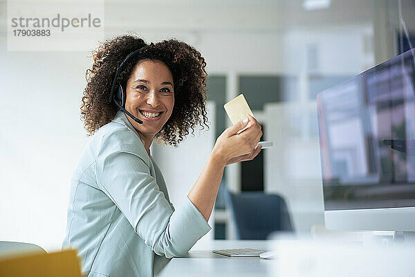 Fröhliche Geschäftsfrau mit Kreditkarte am Arbeitsplatz