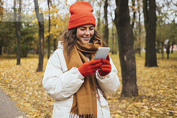 Lächelnde Frau benutzt Smartphone im Herbstpark