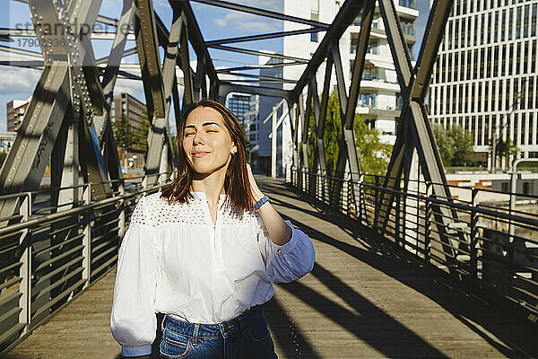 Lächelnde Frau genießt Sonnenlicht auf der Brücke