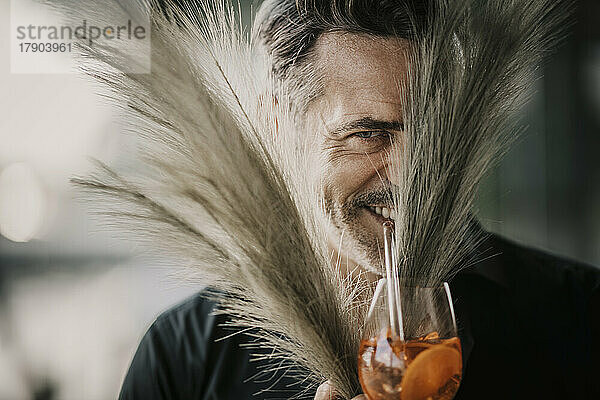Lächelnder reifer Mann beim Trinken und Blick hinter Pampasgras