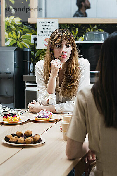 Geschäftsfrau schaut Kollegen beim Diskutieren in der Cafeteria zu