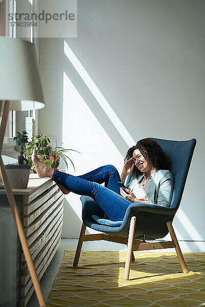 Glückliche Geschäftsfrau mit Mobiltelefon  die auf einem Stuhl sitzt